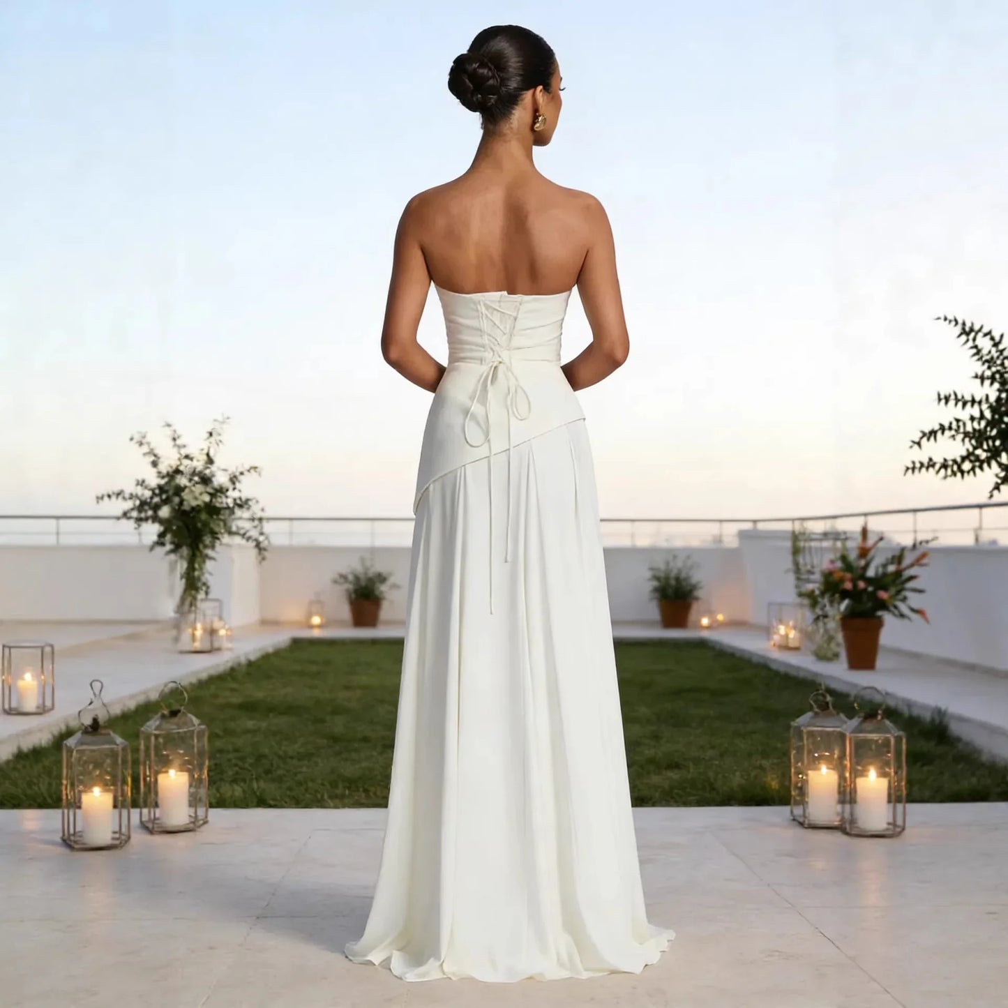 White strapless wedding dress with lace-up back and flowing skirt, shown from behind on rooftop with candle lanterns