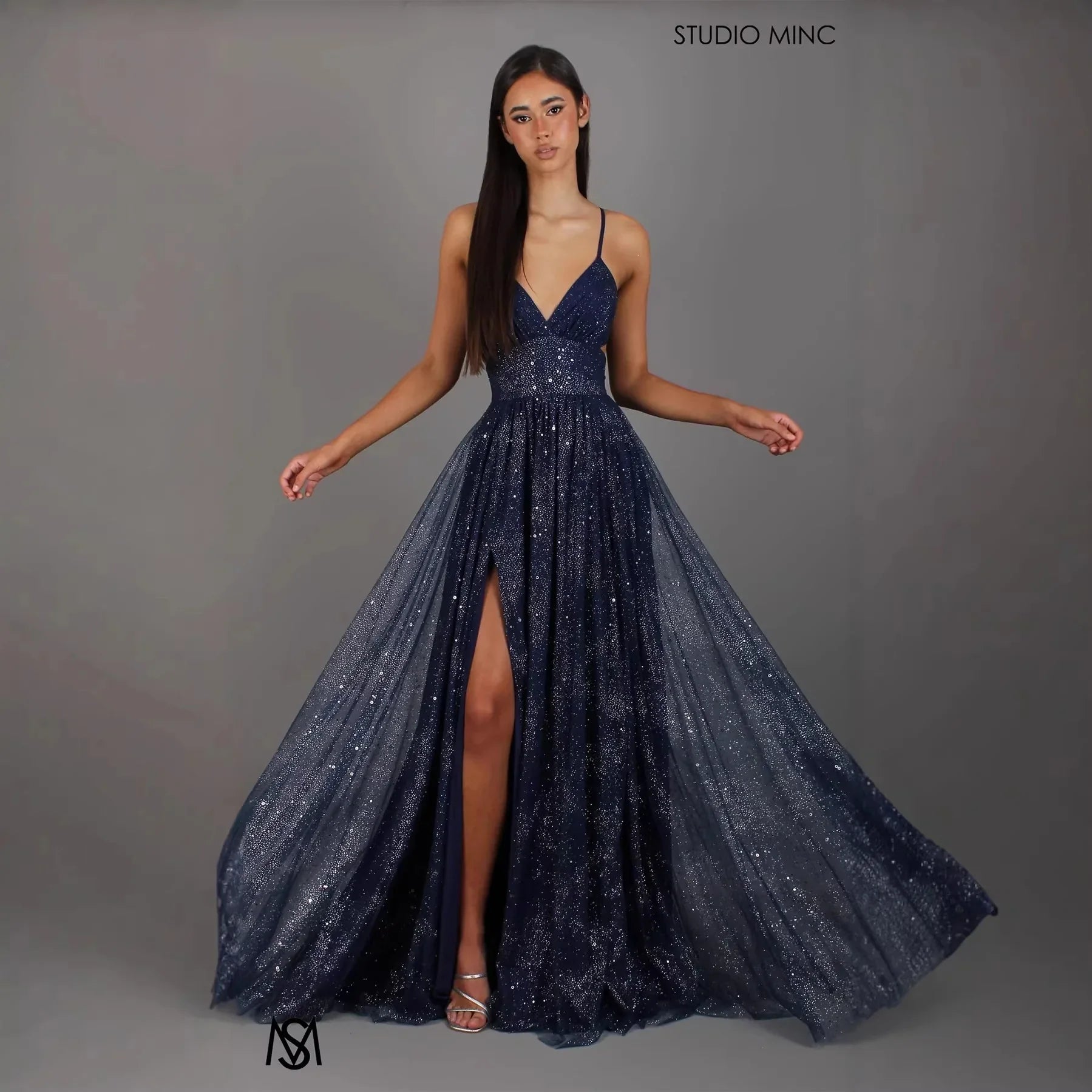Navy blue sparkly A-line evening gown with V-neck, thin straps, and high slit for prom or formal events
