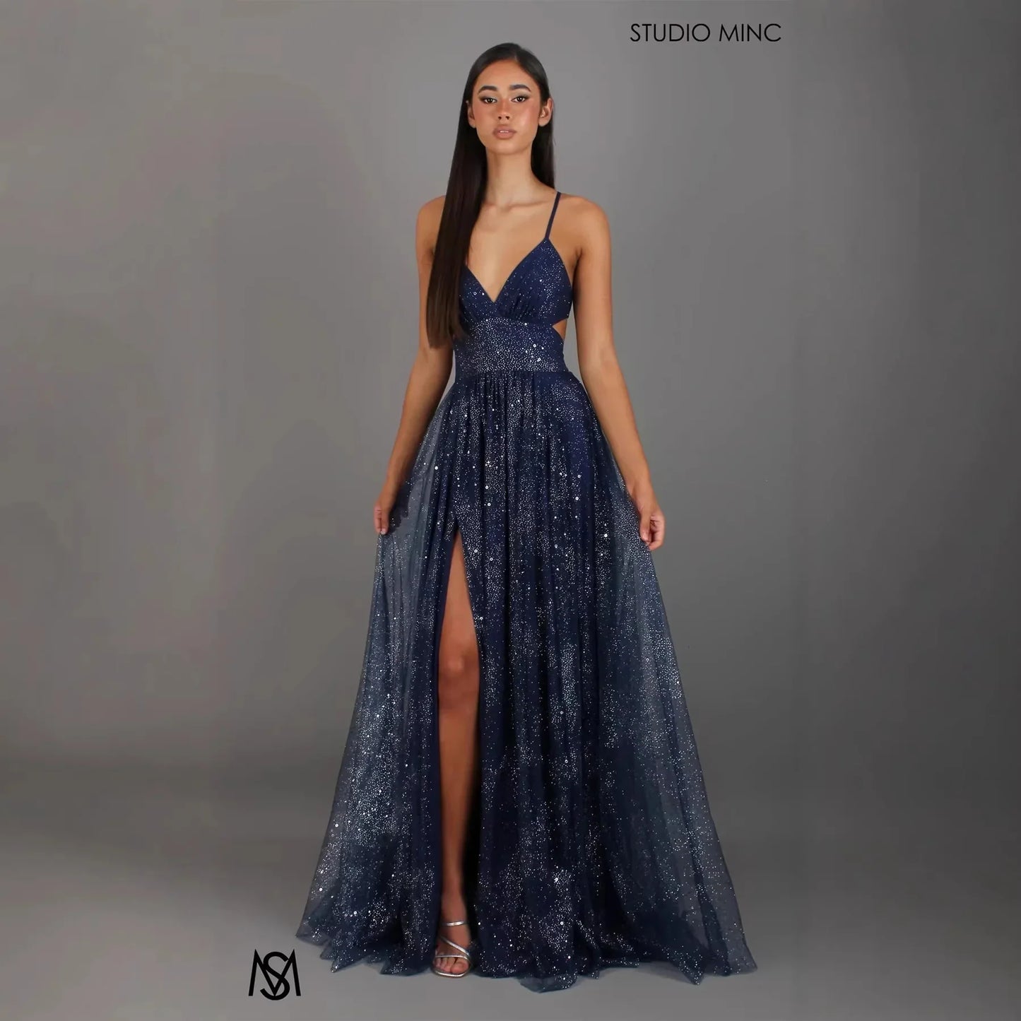 Navy blue sequin evening gown with V-neck, spaghetti straps, side slit, and flowing tulle skirt for formal events